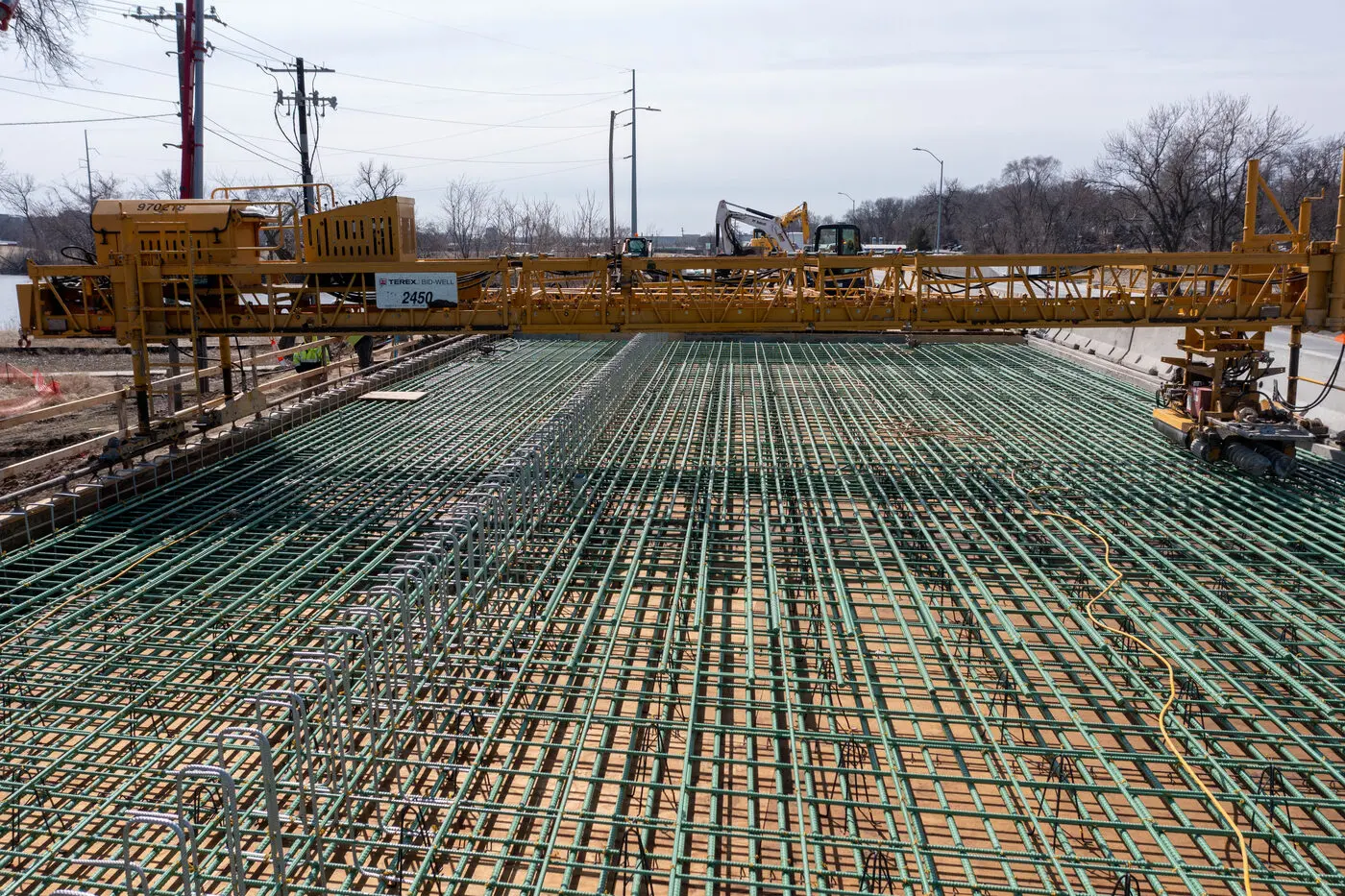 Bridge deck before the pour: epoxy-coated rebar mat across the full deck with a Terex Bid-Well paving machine spanning it
