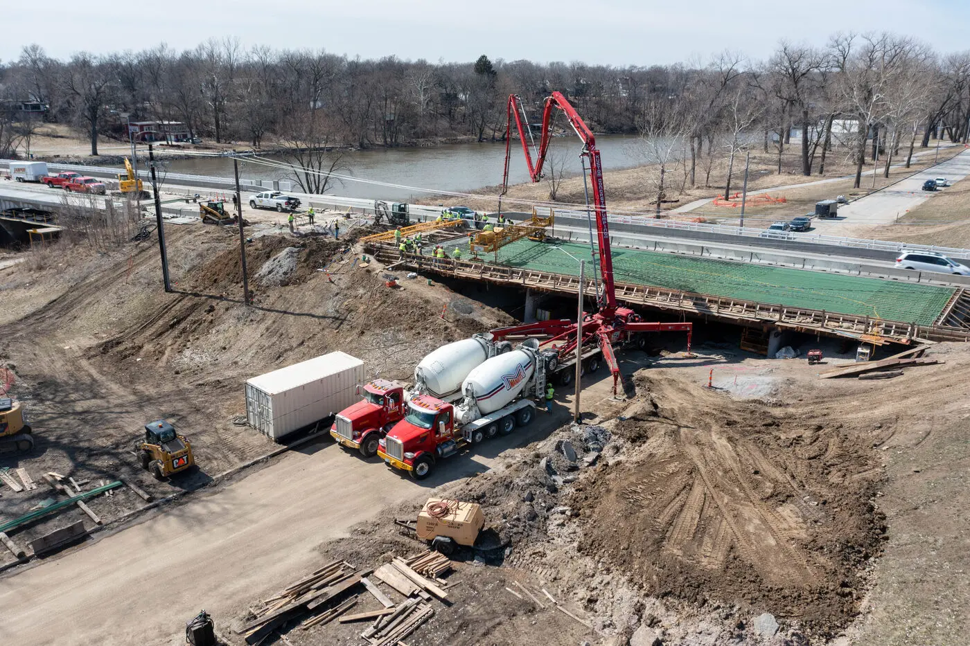 The same bridge deck during the pour, with a concrete pump boom reaching across and mixer trucks feeding it