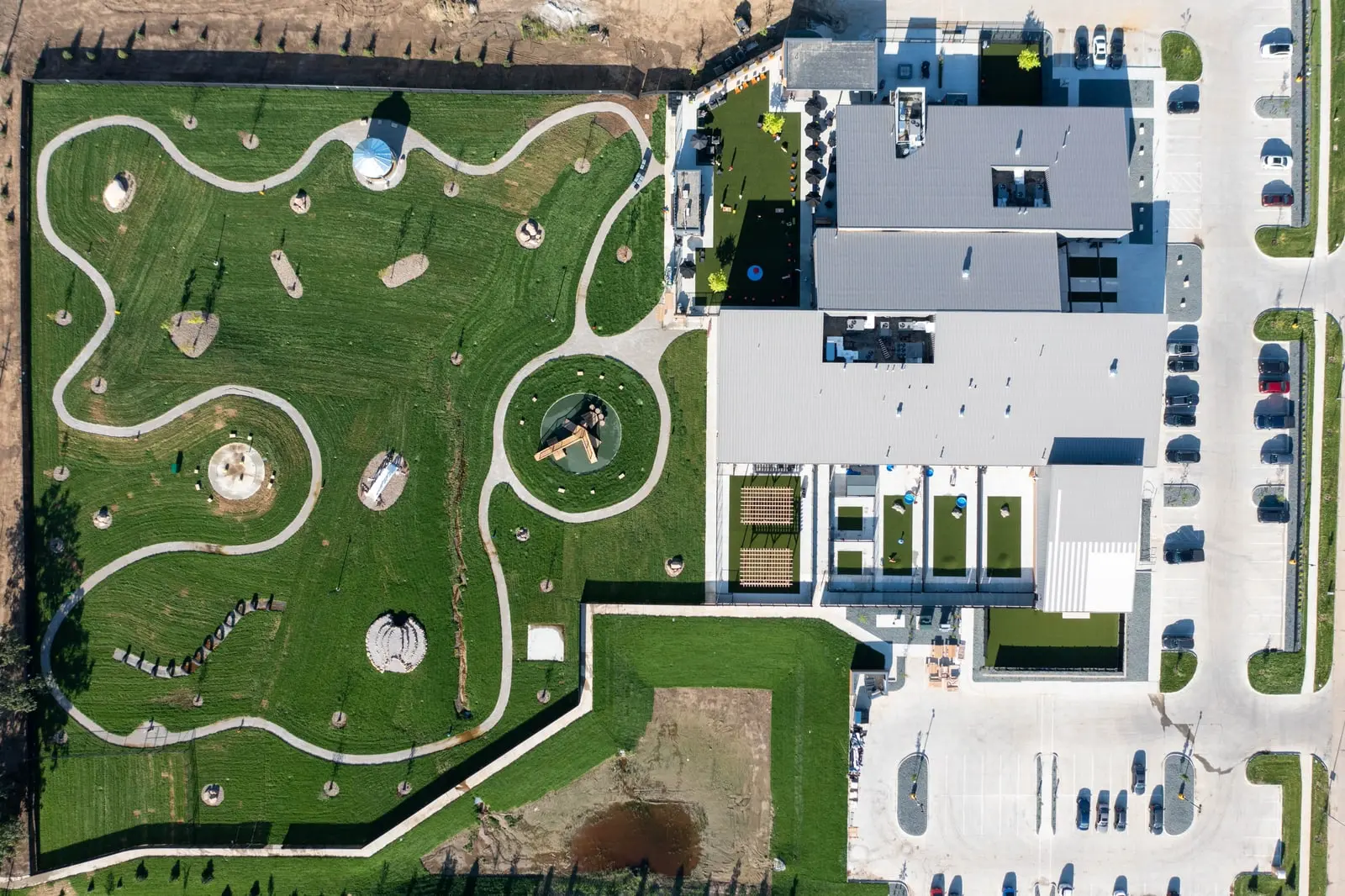 Straight-down aerial of the finished Paws & Pints property: the outdoor dog park laid out as winding white paths through green lawn with circular features, beside the building's turf runs, patio and a full car park