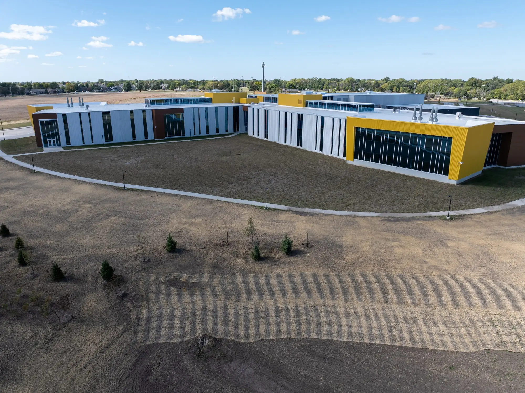 The completed Southeast Polk Middle School in Altoona, Iowa, seen from the air in September 2024 &mdash; a long white and charcoal facade with bright yellow projecting volumes at each end
