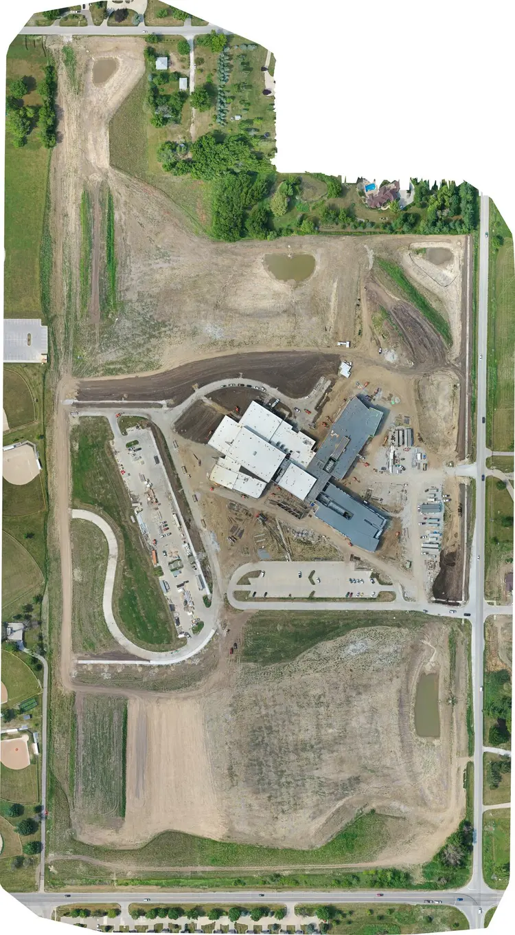 Aerial site map of Southeast Polk Middle School, 27 June 2023 — the structure up and under roof deck, laydown yard along the west edge, drives unpaved and ground bare to the property line