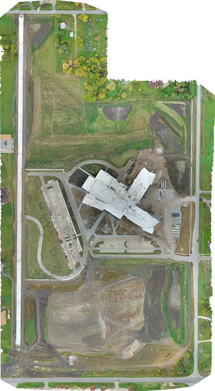 Aerial site map, 15 October 2023 — the building enclosed and roofed, drives and the west lot taking shape, the south field being graded
