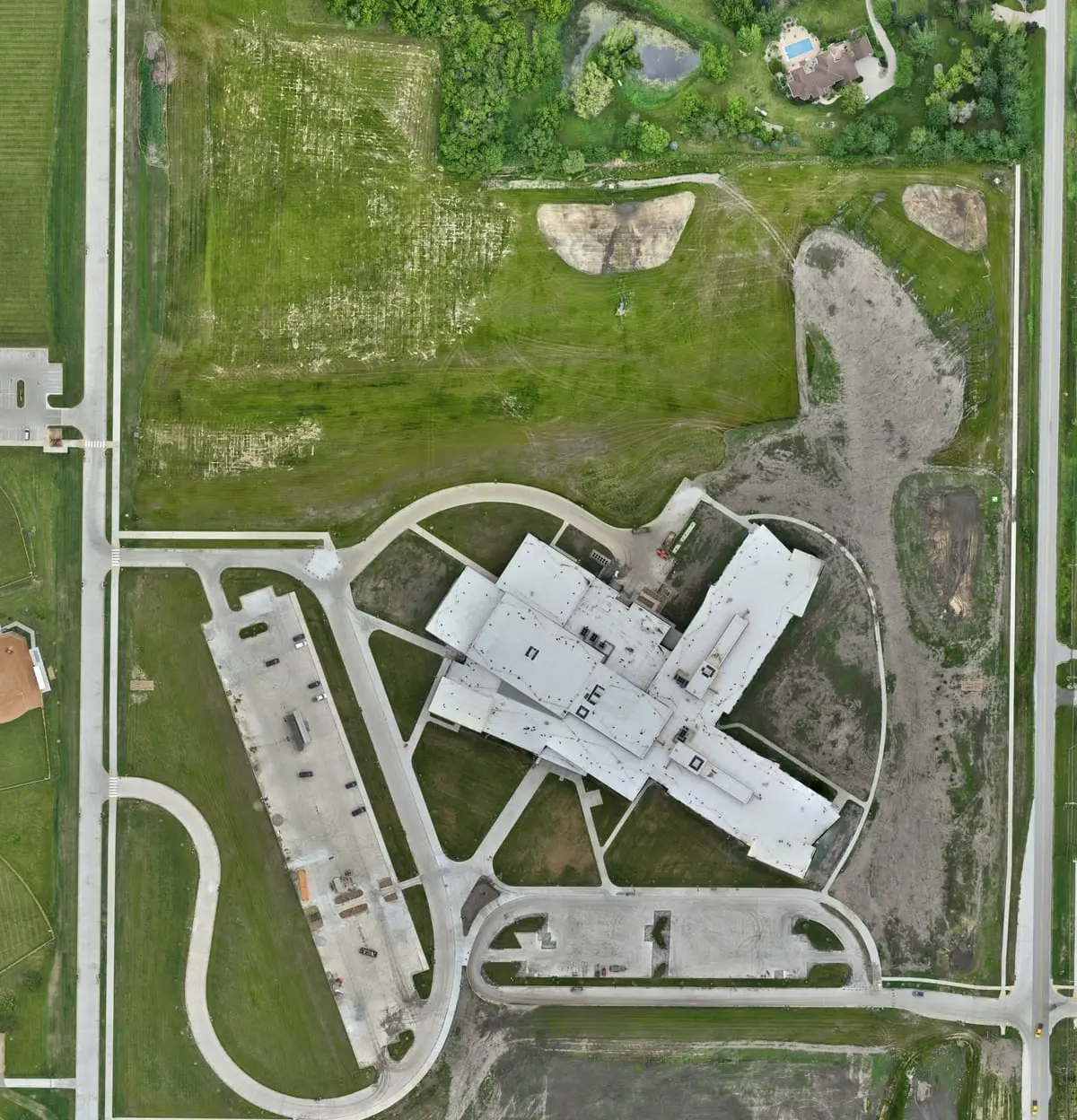 The same ground on 22 June 2024: the finished school, paved and striped lots, completed drives and established grass